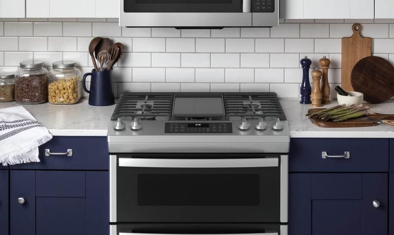Stainless steel slide in range and microwave in kitchen with dark blue cabinets and white marble countertops